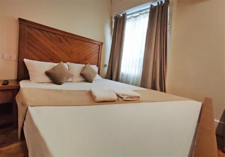 Double bed with a wooden headboard, cushions and curtains