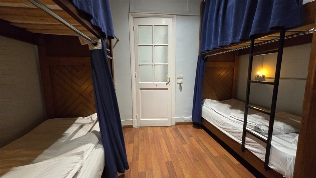 Bunk beds with blue curtains and a lit reading lamp in the dorm