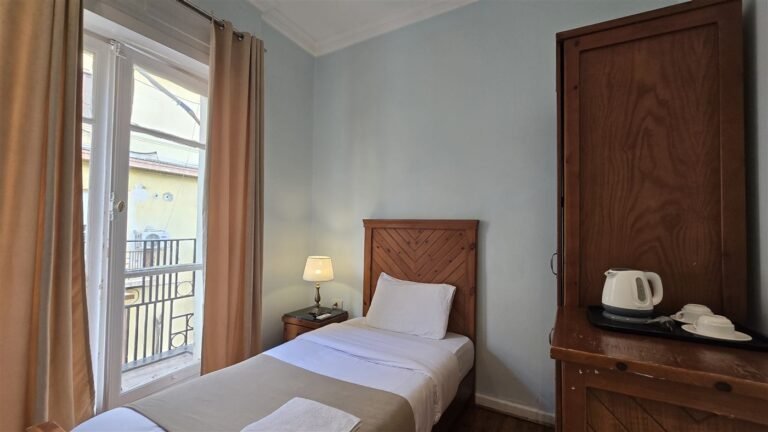 Single room with a wooden bed, a balcony door with curtains and a kettle tray