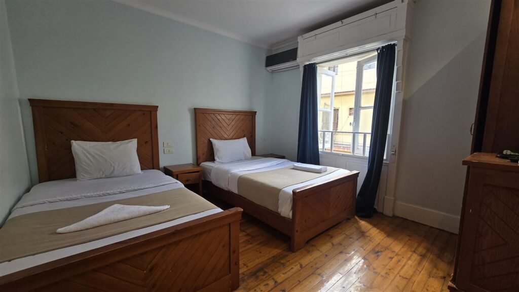 Triple room at Cairo House Hostel with beds, wooden headboards and a window onto the street